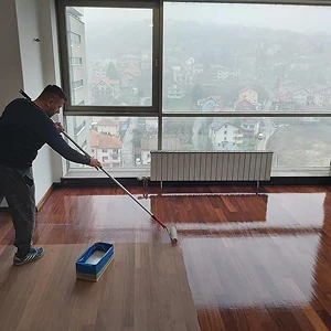 Majstor pažljivo nanosi lak na parket - završna faza obnove drvenog poda